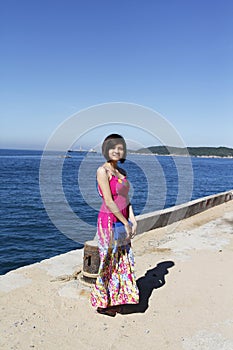 A beautiful girl is standing besides the beach with blue sea and cloud sky