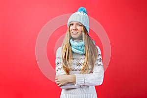 Beautiful girl standing isolated on red background, in warm blue hat and warm scarf