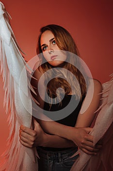 A beautiful girl is standing in jeans with big white wings. On a red background