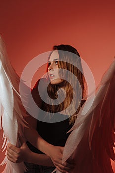 A beautiful girl is standing in jeans with big white wings. On a red background