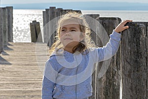 A beautiful girl is standing on an old wooden pier going out to sea.