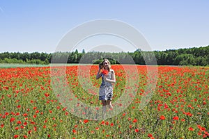 Beautiful girl is standing on summer field full of red poppy flowers in the grass. Sunny day with green lawn background. Happy