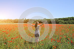 Beautiful girl is standing on summer field full of red poppy flowers in the grass. Sunny day with green lawn background. Happy