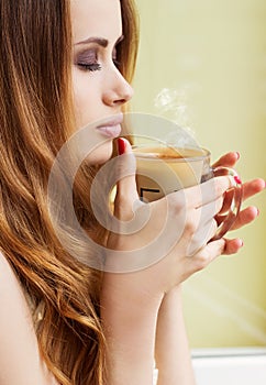 Beautiful girl standing at the window with a hot Cup of invigorating coffee early in the morning