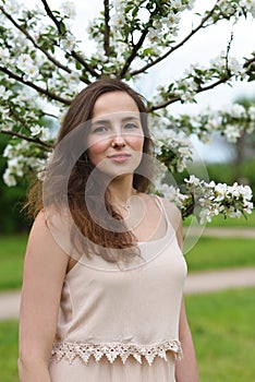 A beautiful girl stands against the background of a young blooming Apple tree