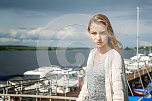 A beautiful girl stands alone on the pier against the background of the watery surface and thunderclouds extending beyond the hori