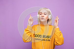 Beautiful girl stands on a blue background in the headphones and listens to music with her eyes closed,wearing orange casual