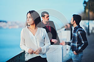 A beautiful girl stands on a bridge at sunset and looks into the distance against a blue sky and an evening city. A young woman in