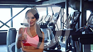 Beautiful girl stands in the gym and shows thumbs up