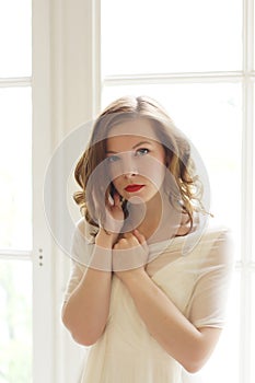 A beautiful girl stands with her back to the window, from which the sunlight pours. Young woman talking on the phone and