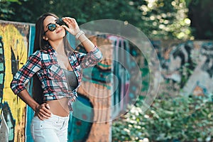 Beautiful girl stands near the wall with graffiti on a warm sunny day. fashion portrait