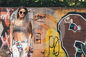 Beautiful girl stands near the wall with graffiti on a warm sunny day. fashion portrait