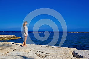 A beautiful girl stands on the rocky shore of the Mediterranean Sea Cyprus.