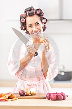 Beautiful girl stands smiling at the camera holding onion in one hand and knife in the other one