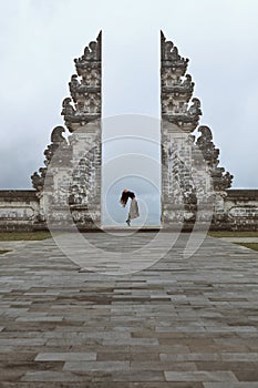 Beautiful Girl Stands On Tiptoes Near Gates Of Heaven In Pura Lempuyang Temple In Bali, Indonesia.