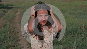 A beautiful girl in the steppe. Slow-motion authentic video. A beautiful young girl straightens her hair, a strong wind