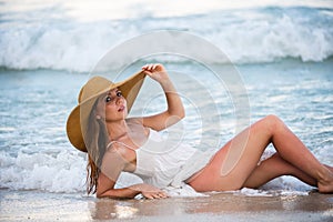 Beautiful girl with straw hat enjoying sunbath at beach. Young tanned woman enjoying breeze at seaside. Carefree woman