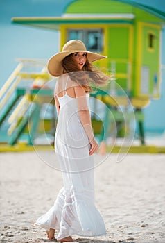 Beautiful girl with straw hat enjoying sunbath at beach. Young tanned woman enjoying breeze at seaside. Carefree woman