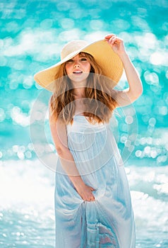 Beautiful girl with straw hat enjoying sunbath at beach. Young tanned woman enjoying breeze at seaside. Carefree woman