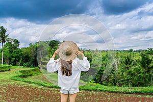 Beautiful girl in a straw hat on rice terraces in Bali. The girl stands with her back to the camera and looks at the