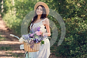 beautiful girl in straw hat and white dress posing with bicycle and flowers