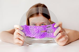 A beautiful girl stretches the purple slime to the sides and hides behind it. Children`s hands play with a slimy toy. Selective