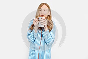 Beautiful girl in striped pajamas, with a Cup in her hands , drinking coffee or tea in the early morning