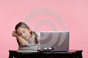 Beautiful girl student fell asleep at work on a laptop on a pink background.