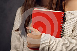 Beautiful girl student in a sweater with a red notebook on a dark backgroundred notebook in the hands of a girl