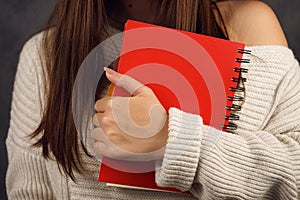 Beautiful girl student in a sweater with a red notebook on a dark backgroundred notebook in the hands of a girl