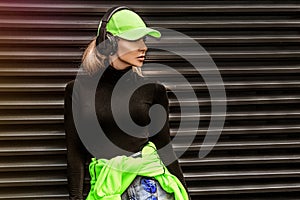 Beautiful girl in stylish sportswear and headphones listens music. Sporty girl in fashion sportswear on the street. Outdoor sports