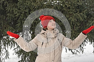 Beautiful girl in stylish winter clothes smiles standing among spruce trees. Young woman enjoys nature of snowy forest