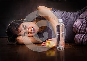 Beautiful girl suffering from anorexy, screaming and laying on the wooden floor with her arms around her head suffering