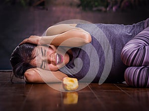 Beautiful girl suffering from anorexy, screaming and laying on the wooden floor with her arms around her head suffering