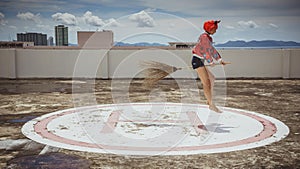 Beautiful girl in a suit devil in a flying broomstick at the helipad. The image of the devil for Halloween. The concept