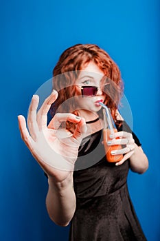 A beautiful girl in sunglasses drinks natural juice, concept of health and lifestyle, shows an OK-gesture with her