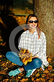 girl in sunglasses sitting under the tree in autumn park