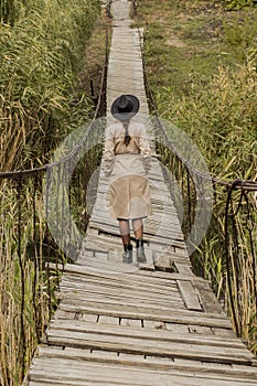 Beautiful girl on a suspension bridge. Woman in a black hat and a beige trench coat. Pretty girl on the suspension bridge. Fashion