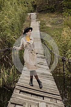 Beautiful girl on a suspension bridge. Woman in a black hat and a beige trench coat. Pretty girl on the suspension bridge. Fashion