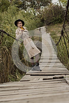 Beautiful girl on a suspension bridge. Woman in a black hat and a beige trench coat. Pretty girl on the suspension bridge. Fashion