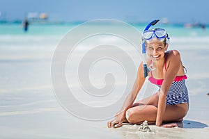 Girl in swimsuit and scuba mask sitting and having fun on tropical beach photo