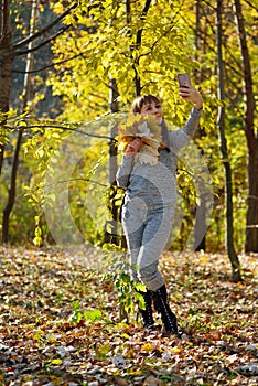 Beautiful girl takes pictures on the phone in the autumn park. Selfie. Wonder autumn. Lifestyle