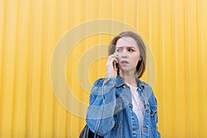 Beautiful girl talking on the phone on a background of yellow wall and looking sideways