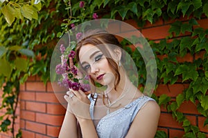 Beautiful girl in tender prom dress on brick wall and green ivy bush with flowers background. Female portrait