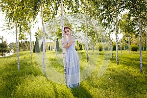 Beautiful girl in tender prom dress among green birch trees. Female portrait