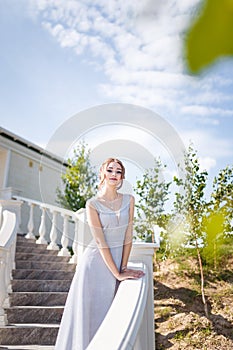 Beautiful girl in tender prom dress on stairs background. Female portrait on spring landscape.