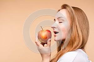 Beautiful girl with tied on back hair eating tasty apple.