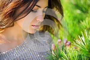 Beautiful girl touches needles on the spruce.