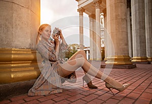 Beautiful girl tourist with perfect legs in stockings shooting with a retro camera outdoor at the old city square