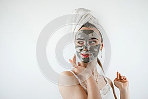 beautiful girl in towel applying black caly mask on face isolated on white gray